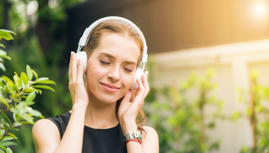 woman wearing black sleeveless dress holding white headphone at daytime