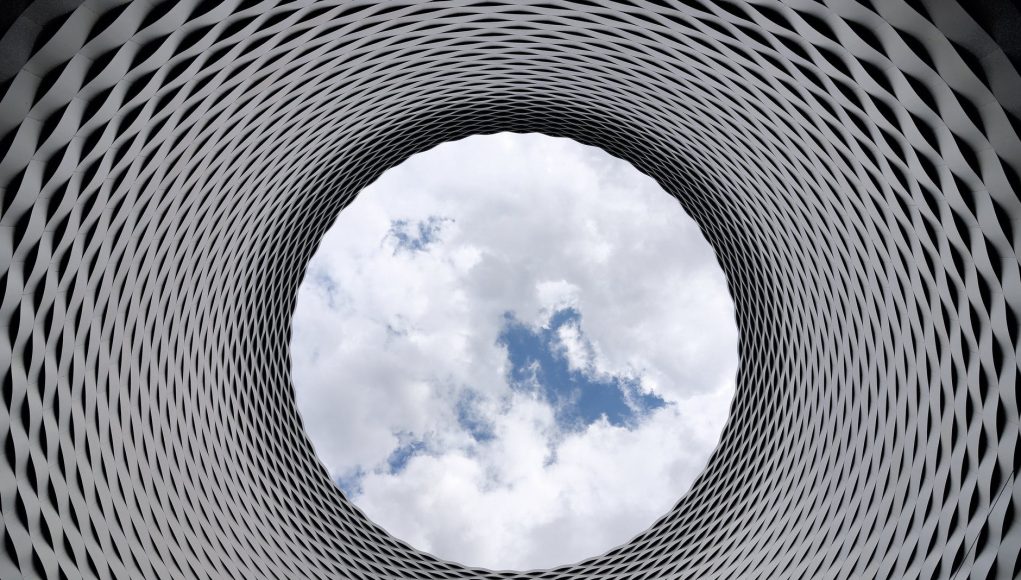 low angle photography of grey and black tunnel overlooking white cloudy and blue sky