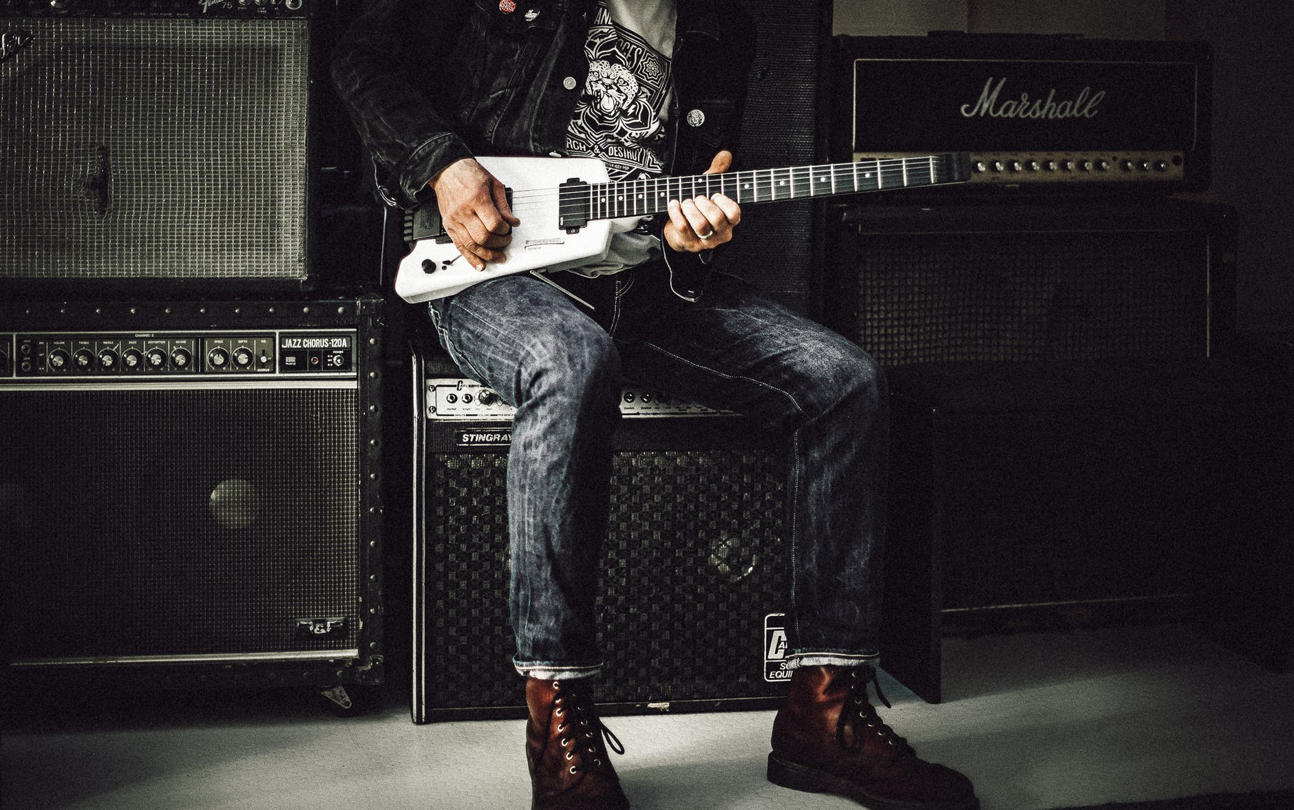 man sitting on guitar amplifier playing electric guitar