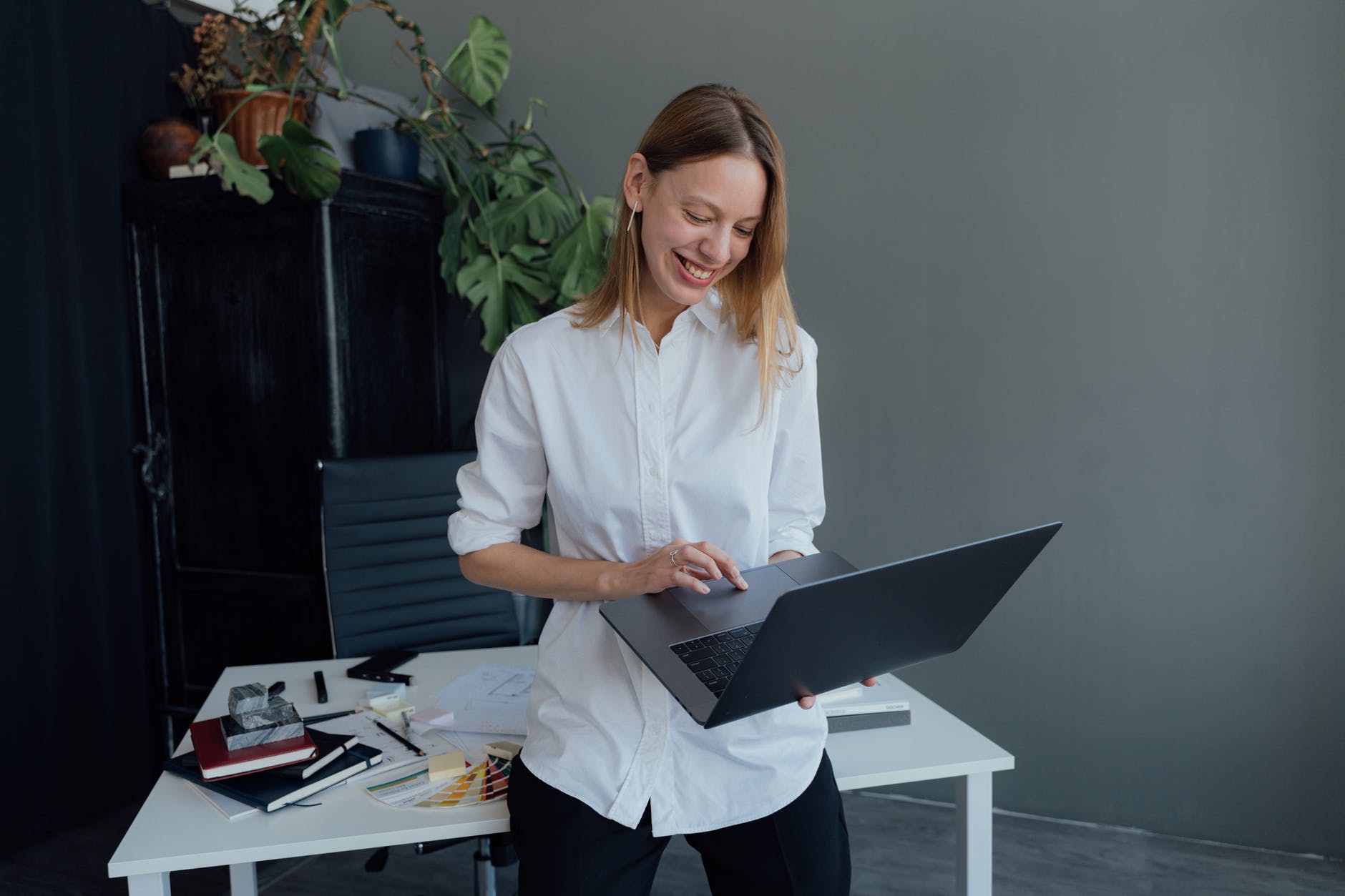 smiling woman using a macbook while leaning on a desk